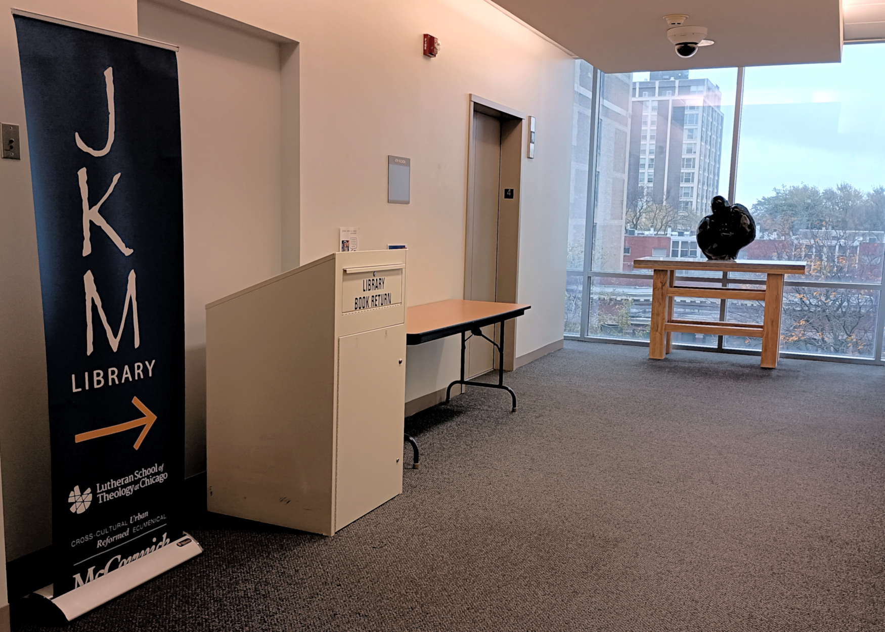 The JKM Library sign, book return, and holds table on the 4th floor of 5416 S Cornell Ave